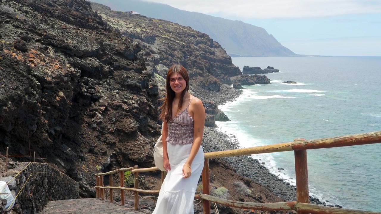 Giovane donna sorridente su un sentiero costiero con vista sull'oceano.