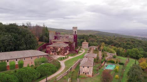 Flying-towards-beautiful-fairytale-castle-on-hill-surrounded-by-woodland-on-cloudy-day,-aerial