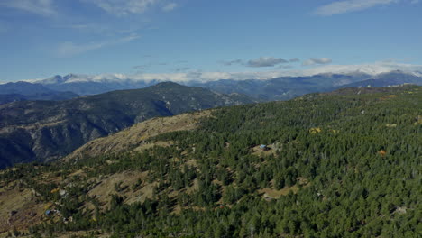 aerial moving past cabin on mountainside towards peaks in distance, 4k