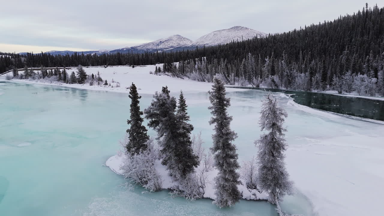 An aerial establishing shot captures the frozen Lake Kusawa and Takhini River winding through snow-covered fir forests with mountains on the horizon, epitomizing a pristine Yukon winter wilderness.