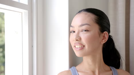 a young biracial woman with a joyful expression stands near a window with copy space