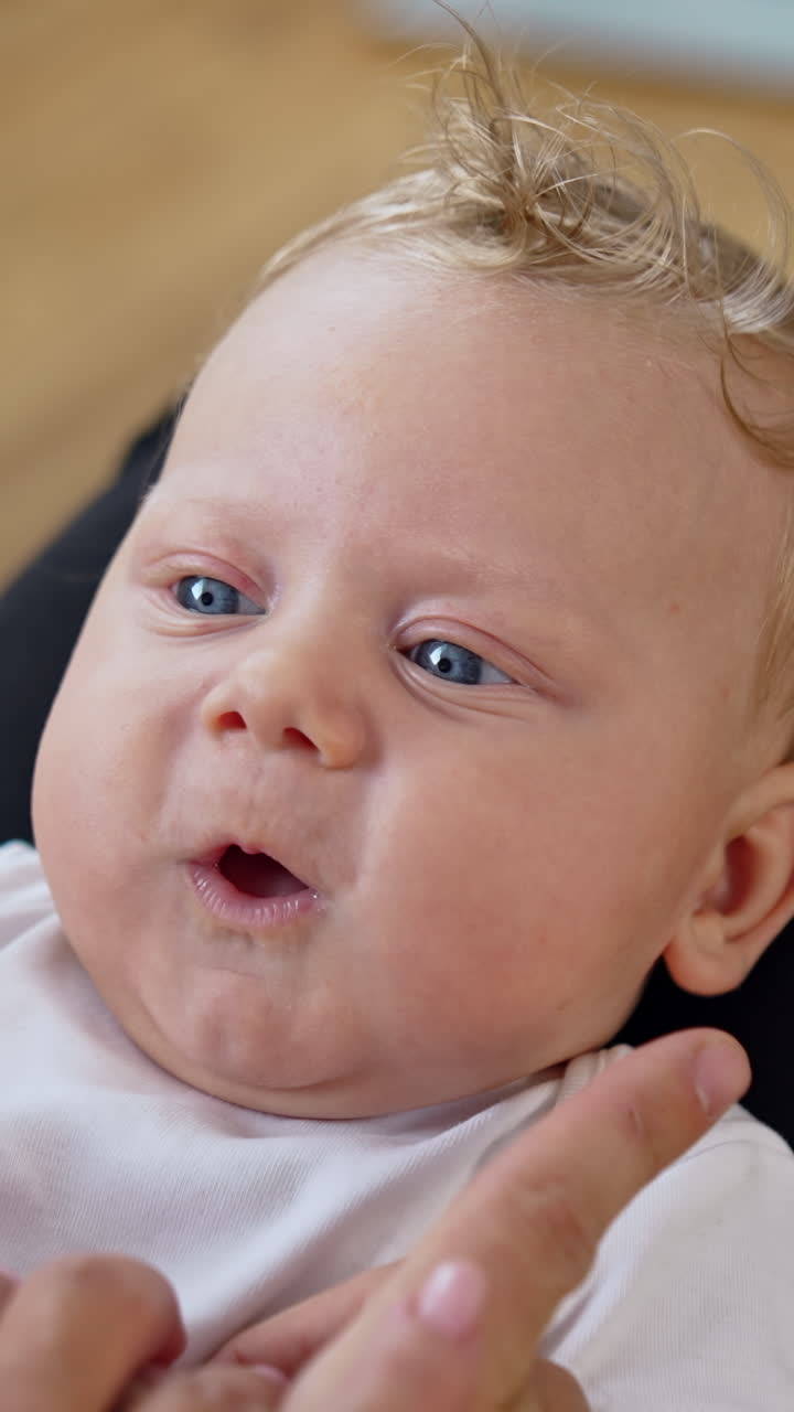 Parents play with their adorable baby. Dad's fingers touch cute plump kid's cheeks. Close up. Vertical video
