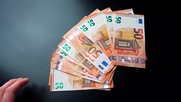 Draufsicht von Händen, die 50-Euro-Banknoten von einem Stapel auf einem dunklen Schreibtisch mit Textfreiraum nehmen. Konzept für Zahlungen, Budgetplanung, Sparen und persönliche Finanzen.