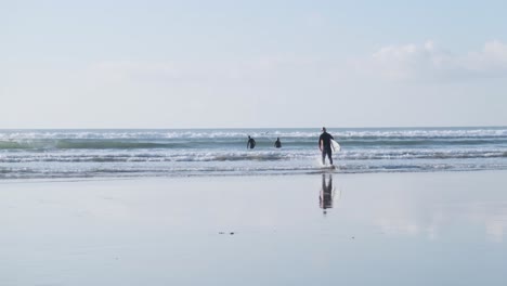 surfers walking into the water with their boards under their arms