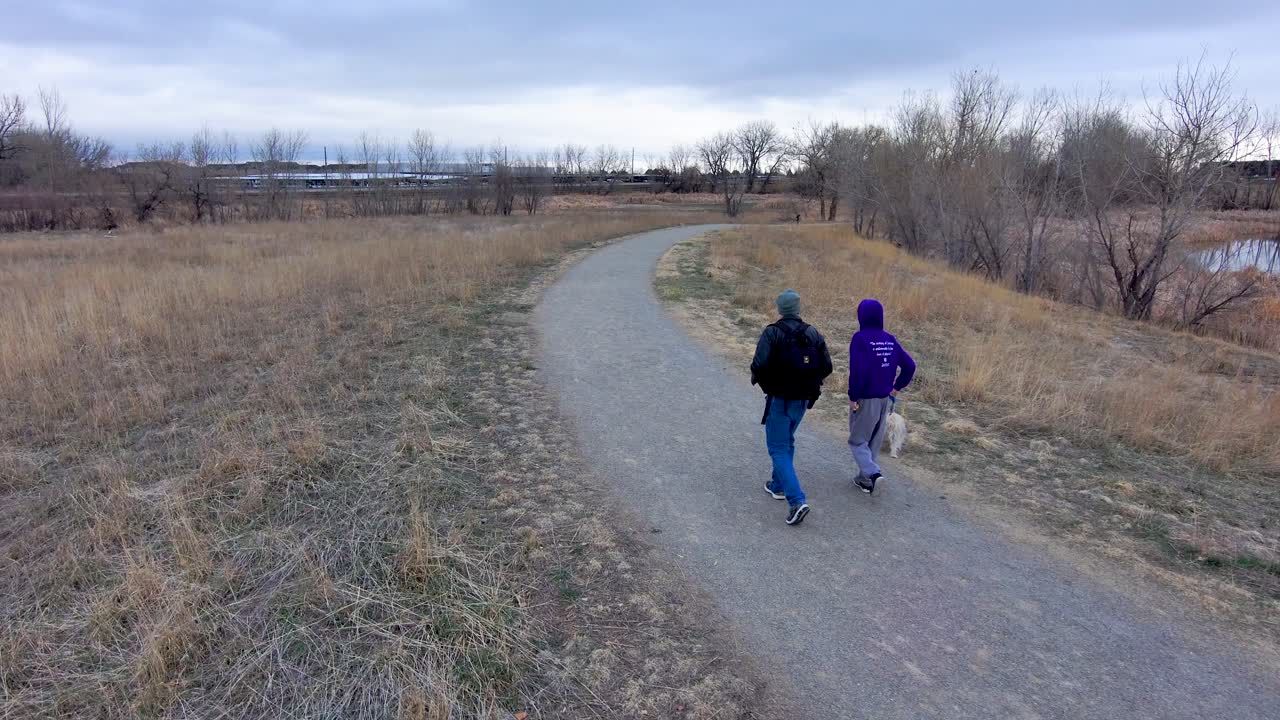 A wintry path is the destination for a  man and his son as they walk a tiny dog along its bleak length.