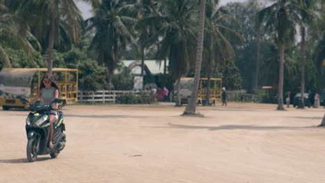 Una-Chica-Monta-Una-Motocicleta-Negra-En-Una-Plaza-Entre-Palmeras-Tropicales