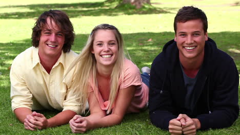 woman laughing while lying on the grass before her friends roll in next to her