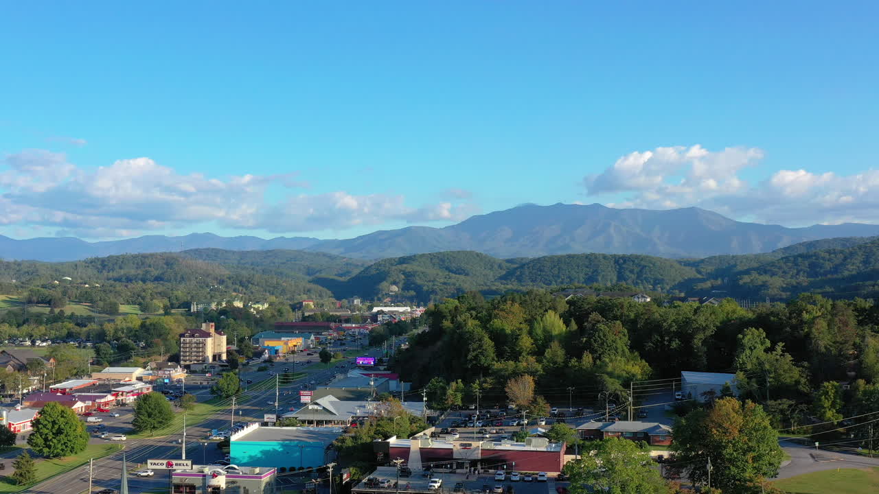 Dramatic aerial retreat revealing a charming Tennessee town unfolding against the majestic Great Smoky Mountains. Captures the allure of mountain vistas and lively streets