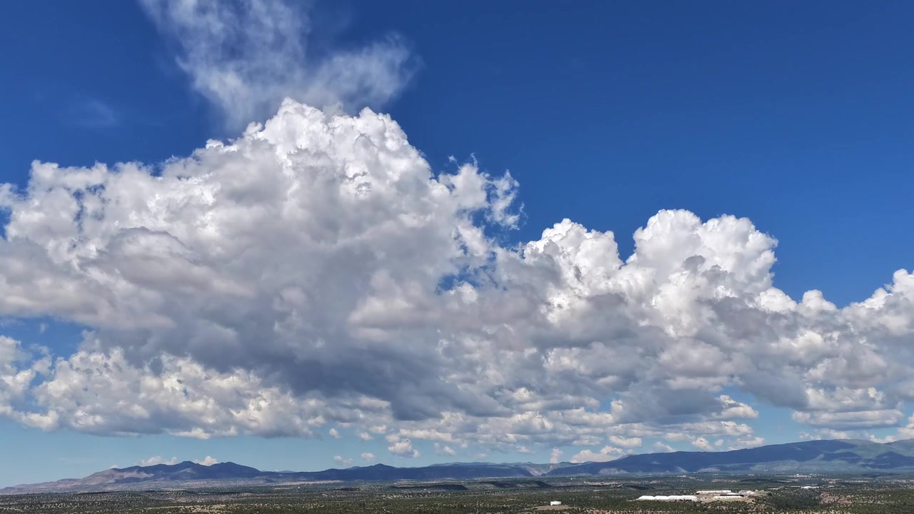 4K UHD drone-timelapse, der fanger lyse hvide cumulusskyer, der hurtigt bevæger sig hen over en dybblå himmel. Store skygger fejer hen over den flade kratlandskabsmåde og fjerne bjergtoppe