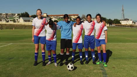 Female-soccer-team-standing-arm-to-arm-on-soccer-field.-4k