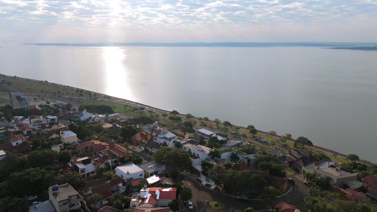 Sorvolo panoramico di un drone sul paesaggio costiero di Posadas con case e luce solare che si riflette sulla superficie dell'oceano, Misiones, Argentina