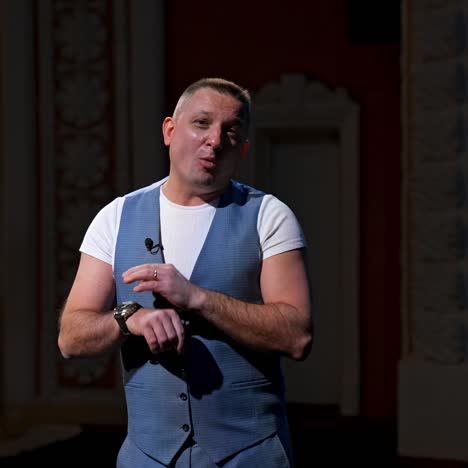 public speaker gives performance. middle age male entertainer, presenter or actor on stage. man in theater wears handfree microphone