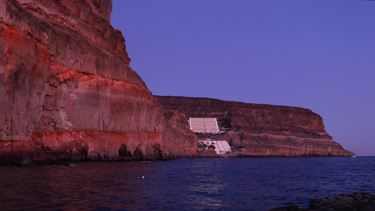 Cliffs lining the island and middle-lying complex of buildings on the rock during sunset with reflection on sea surface 4k slow motion capture at 60fps.