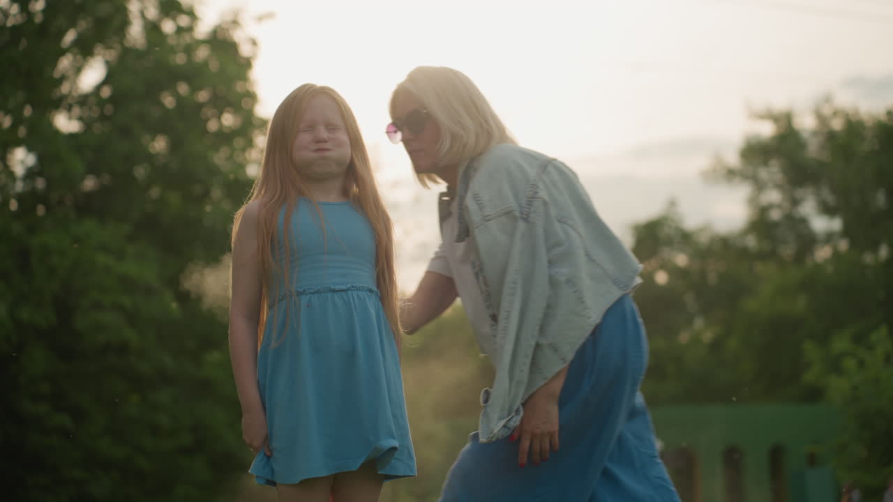female toddler squinting and puckering face while guardian sprays insect mist near her, backlit park setting, summer outdoor care moment showing playful discomfort and protective routine