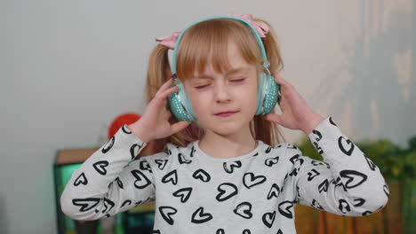 niña feliz niña con auriculares bailando y saltando mientras escucha la música en casa sola