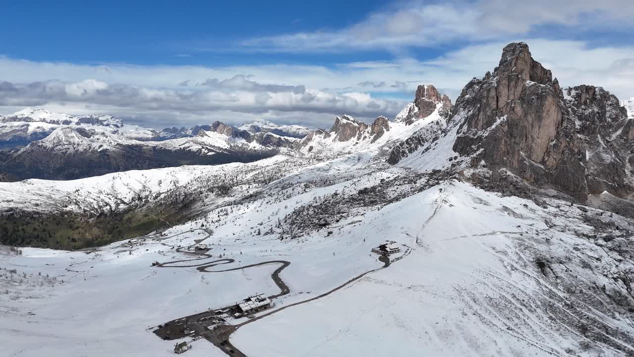 Aerial drone view of Passo di Giau winding through snowy Dolomites with rugged peaks in the background