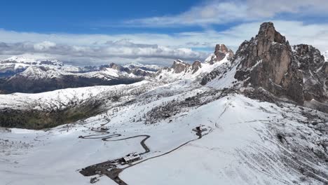 Aerial drone view of Passo di Giau winding through snowy Dolomites with rugged peaks in the background