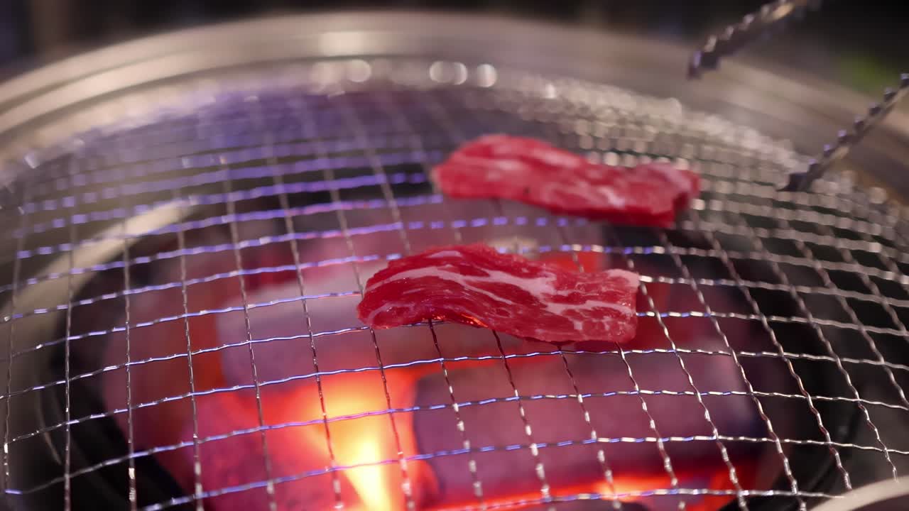 Close-up view of beef slices sizzling over a glowing charcoal grill, highlighting the cooking process.