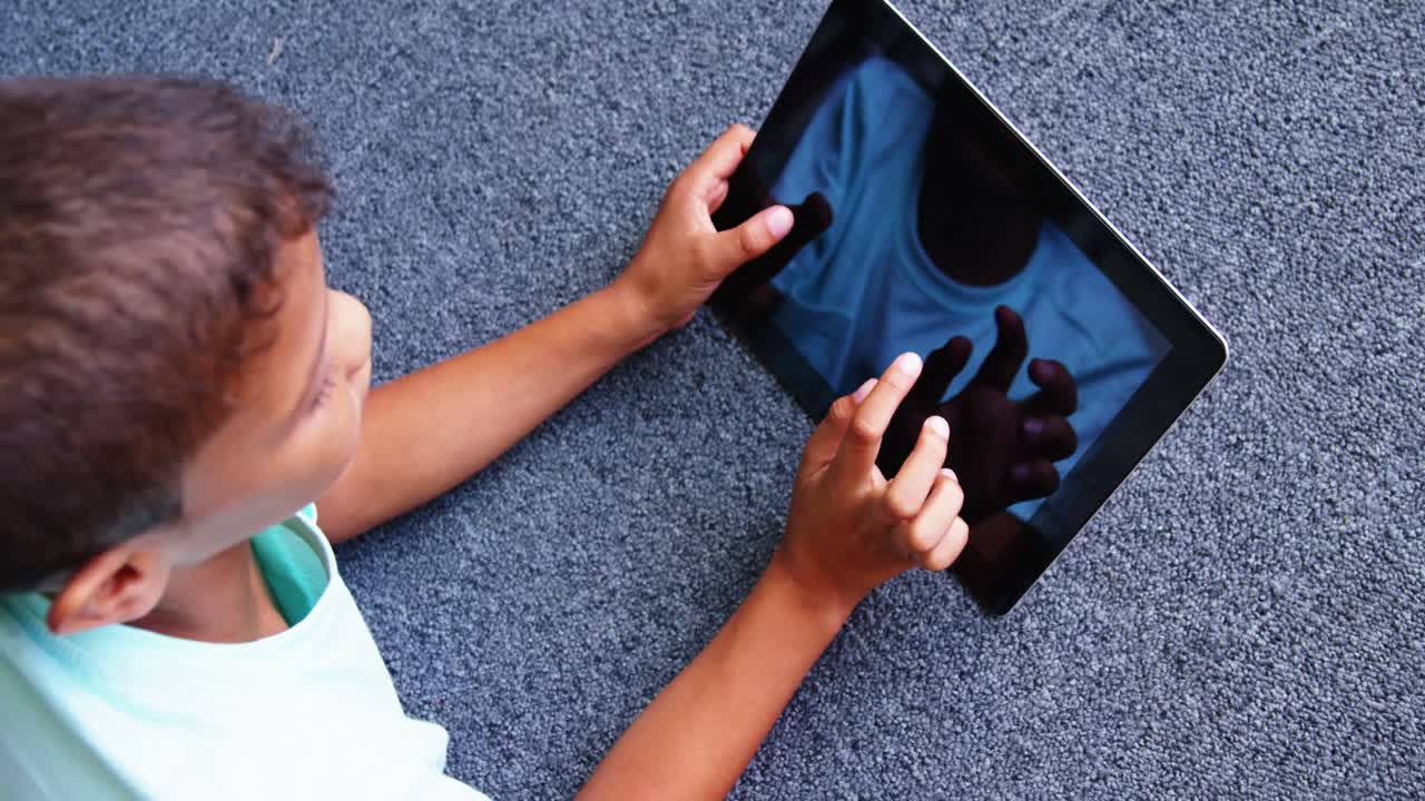 Studente sdraiato a terra che usa un tablet digitale nella biblioteca scolastica