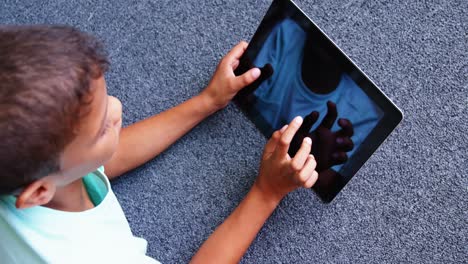 Schoolboy-lying-on-floor-and-using-digital-tablet-in-library-at-school