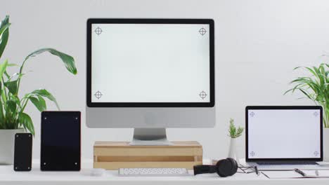 video of laptop, smartphone, tablet and computer on wooden table with copy space in office