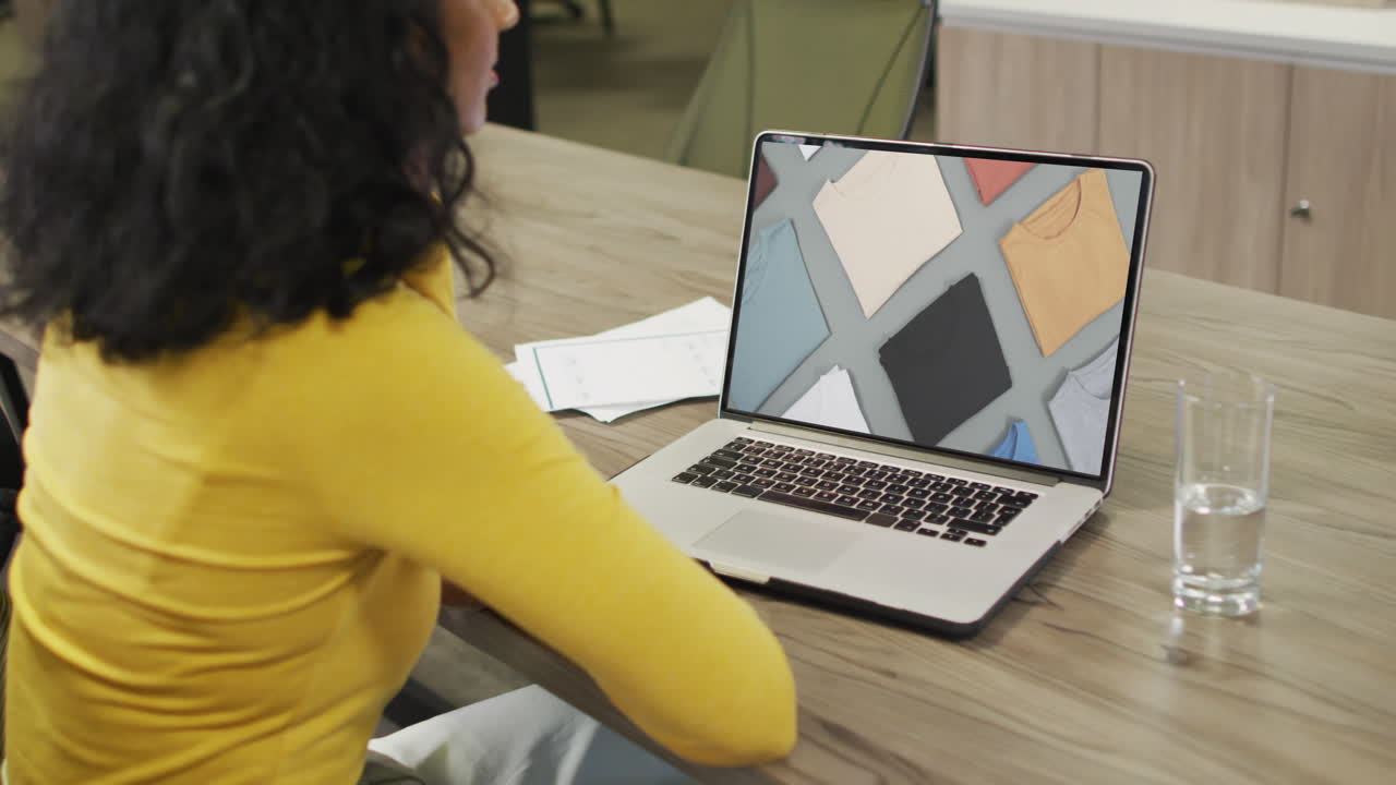 mujer biracial en la mesa usando portátil, compras en línea de ropa, cámara lenta