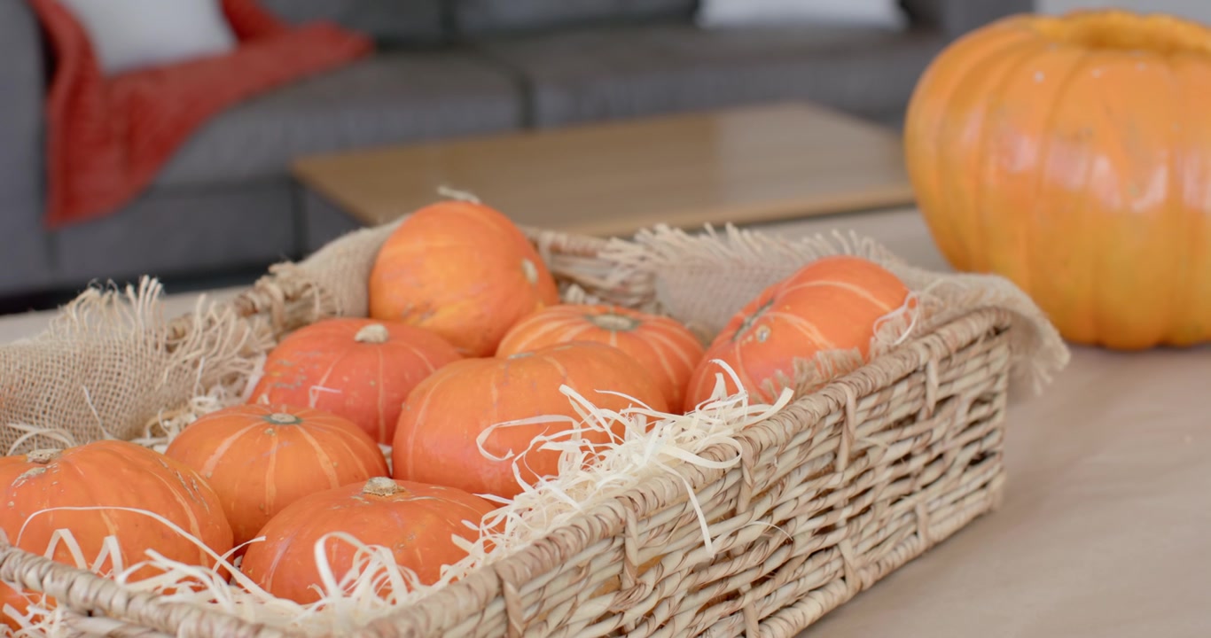 Camera is pulling back, panning to reveal woven basket with mini pumpkins on table, halloween decor