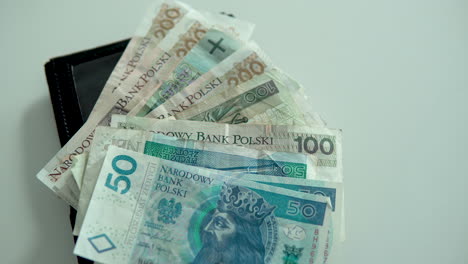 various denominations of polish banknotes on top of a black leather wallet - overhead panning shot