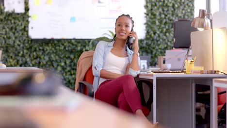Mujer-De-Negocios-Informal-Afroamericana-Hablando-Por-Teléfono-Inteligente-En-La-Oficina,-Cámara-Lenta