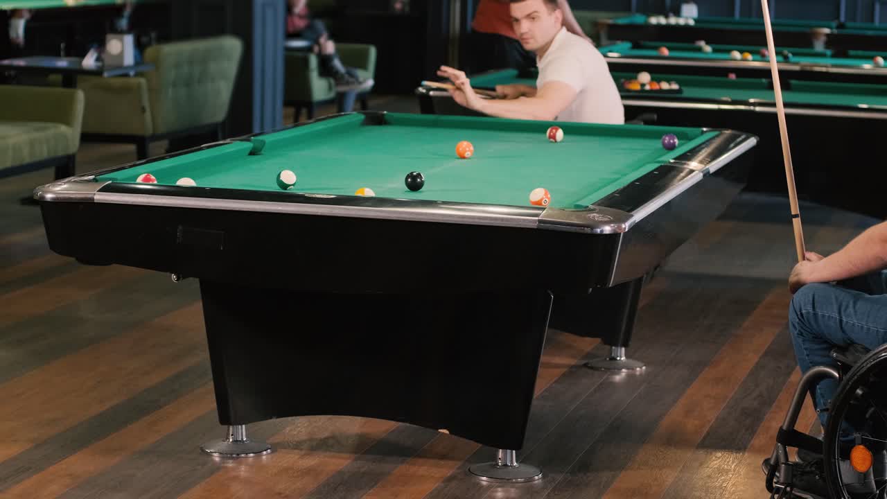 Adult men with disabilities in a wheelchair play billiards in the club