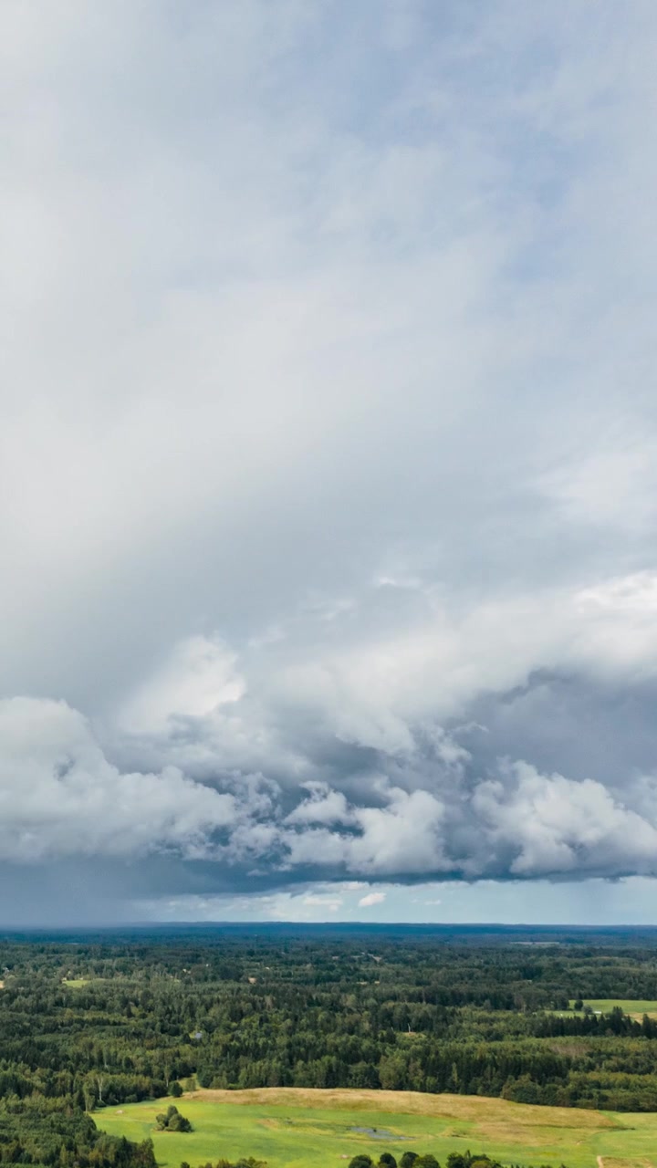 Vertical drone hyperlapse of dramatic rain clouds and storm front moving over green rural landscape.