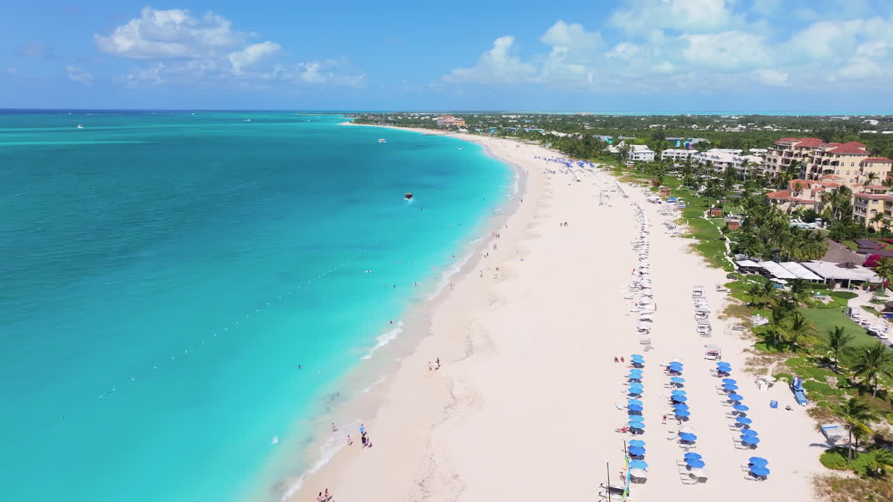 Forward aerial 4K footage showcasing the stunning coastline of Grace Bay Beach with white sand, blue waters, and green coastal resorts