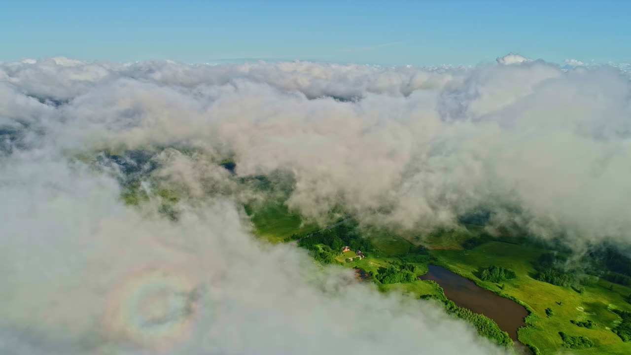 Drone flying over clouds capturing green pasture land during daytime. Cloudscape.