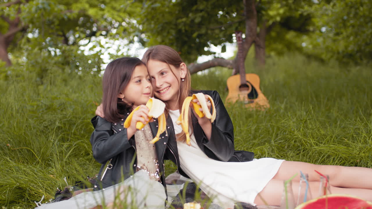 두 소녀 가 공원 에서 바나나 피크닉 을 즐기고 있다