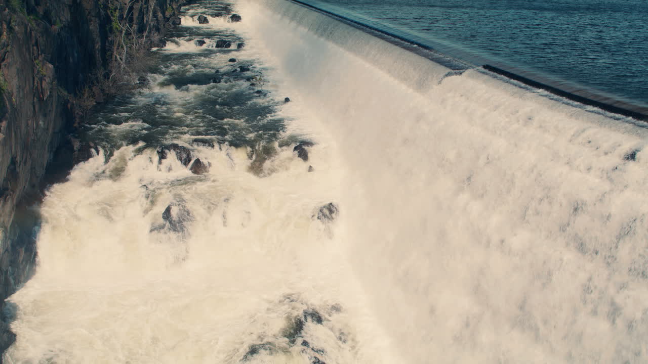 Wide shot of white water rushing down New Croton Dam stepped spillway and gorge waterfall with sun light getting brighter. Static shot, Slow motion 40 fps.