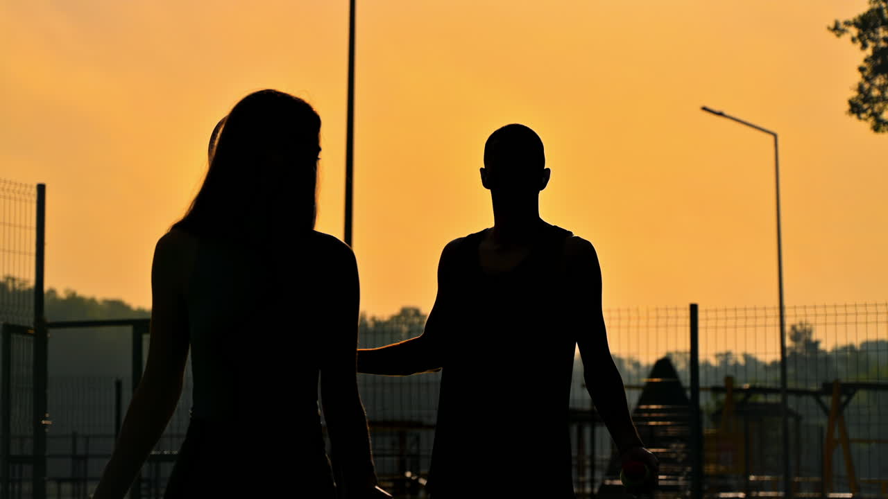 A man and a woman playing tennis at sunset, after rain