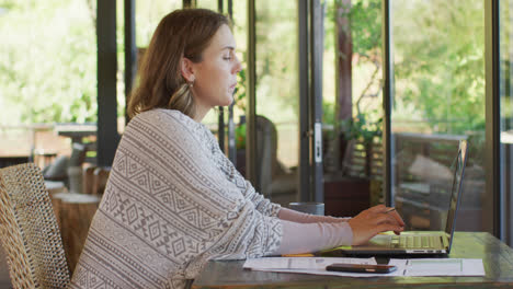 Mujer-Embarazada-Caucásica-Sentada-En-El-Escritorio,-Trabajando-Remotamente-En-Una-Computadora-Portátil