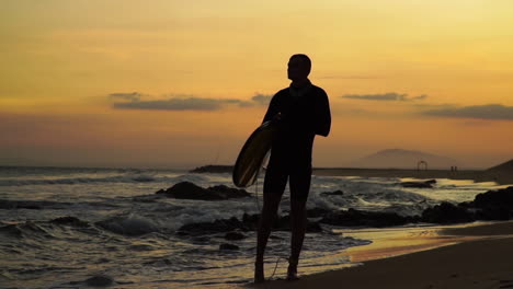 Silueta-De-Un-Tipo-Con-Una-Tabla-De-Surf-Al-Atardecer-Disparada-En-Cámara-Lenta