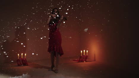 mujer tocando el violín en un vestido rojo con copos de nieve y velas