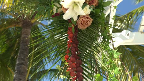 Slow-push-in-revealing-beautiful-colors-of-floral-arrangement-hanging-on-post-with-palm-trees-in-the-background