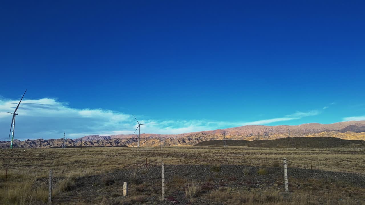 Along the Way, Qinghai and Gansu Province, China - Wind Turbines Rise Over a Wide, Dry Plain Backed by Rugged, Sunlit Mountains Under a Deep Blue Sky - POV Shot