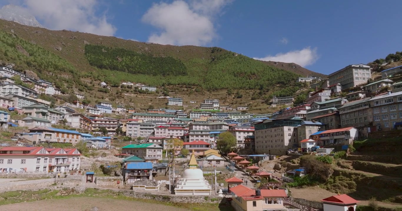 Namche Bazaar, Everest, Nepal'de, parlak güneşli bir günde yemyeşil tepelerin arasına yerleşmiş modern pansiyonların ve otellerin havadan uzaklaşan çekimi.