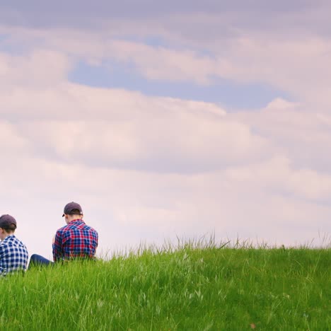 Two-Teenage-Boys-Are-Sitting-On-A-Green-Meadow-Using-Mobile-Phones-1