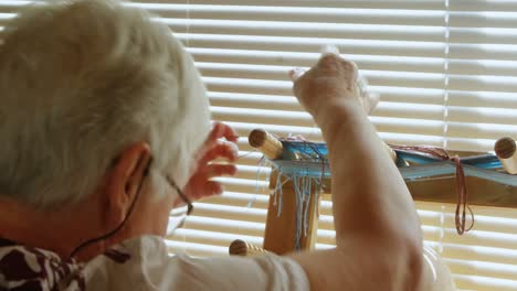 Rear-view-of-old-caucasian-senior-woman-preparing-and-standing-at-hand-loom-machine-in-a-workshop-4k