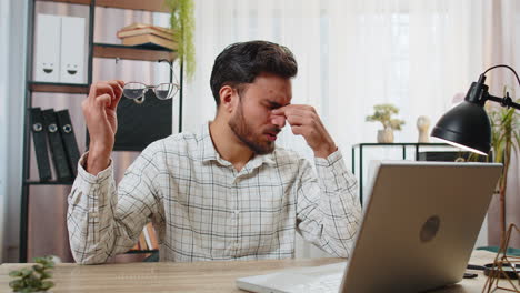 Overworked-young-Indian-bearded-businessman-suffering-from-eye-strain-and-headache-working-on-laptop