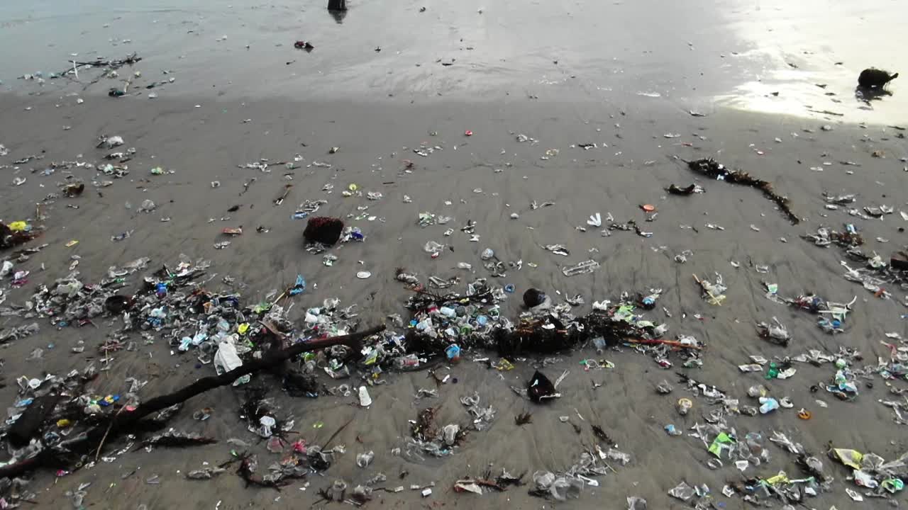 Tilt up shot from a heavily polluted beach to the ocean, as waves washing trash to the shore