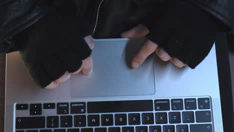 shot looking down at persons hands in black gloves typing on a laptop, then camera tilts up to reveal terrorists eyes