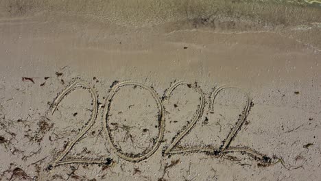 large twenty twenty written in the sand at the bottom of the frame as water laps onto the beach