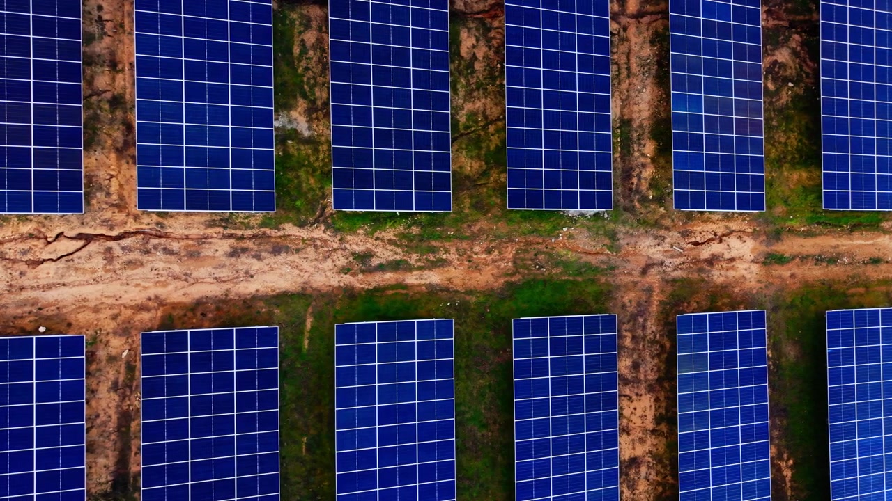 File parallele di pannelli solari attraverso un campo pianeggiante, Bulgaria. Vista con drone quasi dall'alto di moduli densi blu scuro in linee orizzontali diritte con stretti intervalli di terreno arancione ed erba verde.