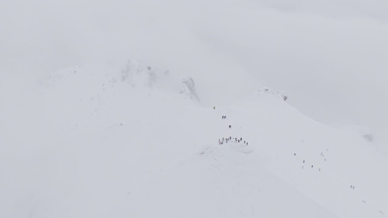 Kış mevsiminde karla kaplı Ciucas zirvesinde yürüyüş yapan insanların havadan drone görüntüsü. Romanya, Karpat Dağları.